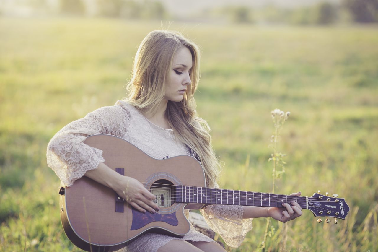 A serene scene of a woman playing a guitar outdoors in the countryside during daytime.